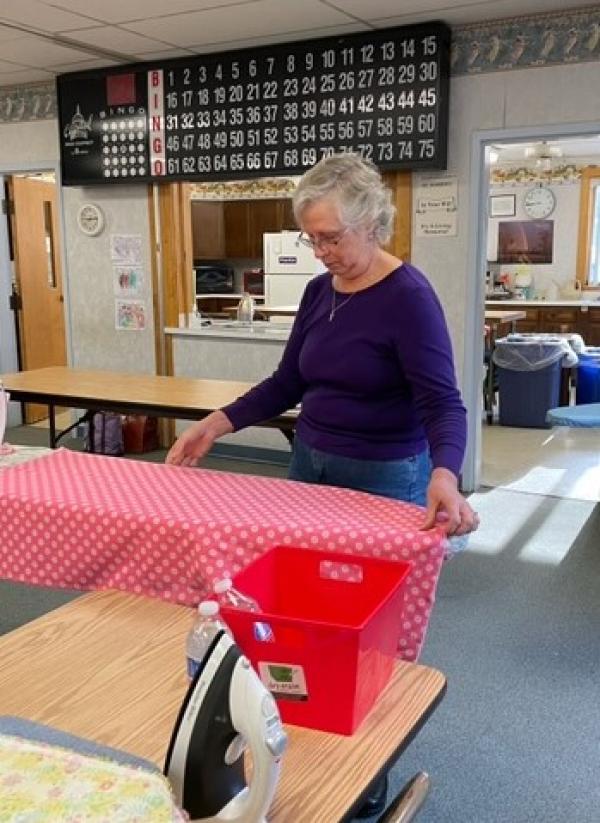 St. Veronica's Treasurer, Robin Gauthier, presses material as the first step in preparing fabric for dress making.